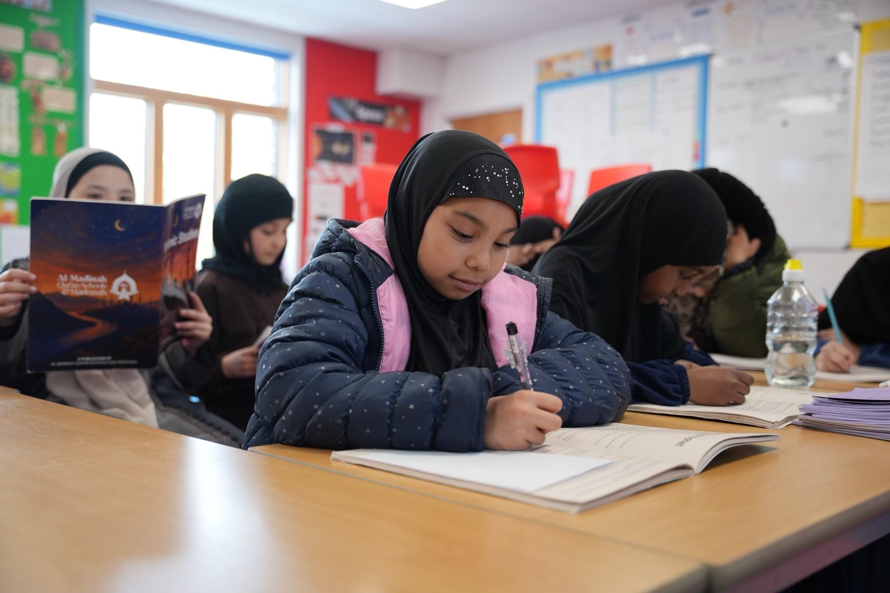Students writing in their books during a madrasah lesson